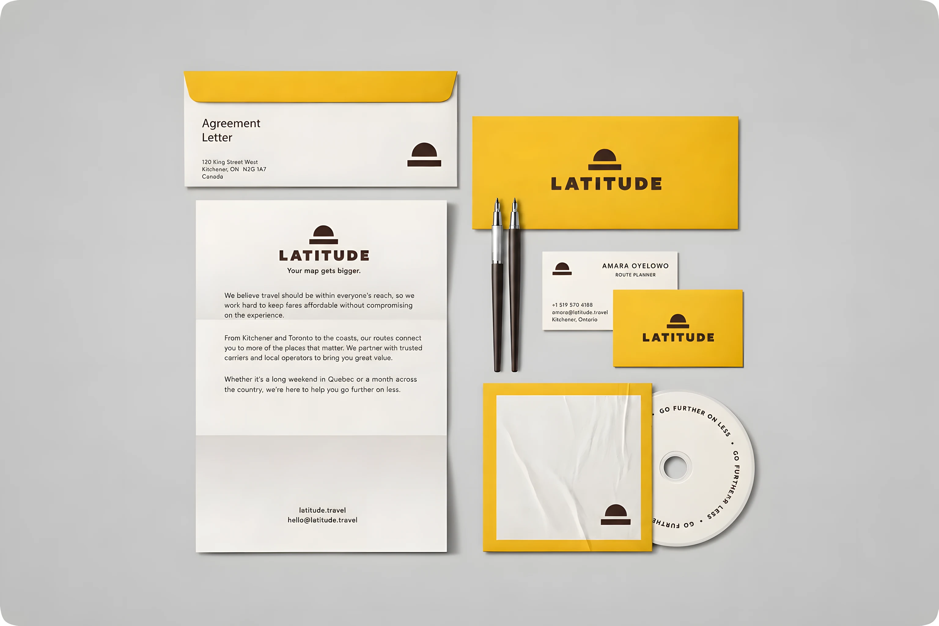 A stationery flat-lay on grey: a porcelain letterhead and agreement envelope with a yellow flap, a golden yellow envelope carrying the Latitude lockup, two business-card faces — one with a route planner's name and Kitchener contact details, one plain yellow with the lockup — two pens, and a disc sleeve printed GO FURTHER ON LESS.